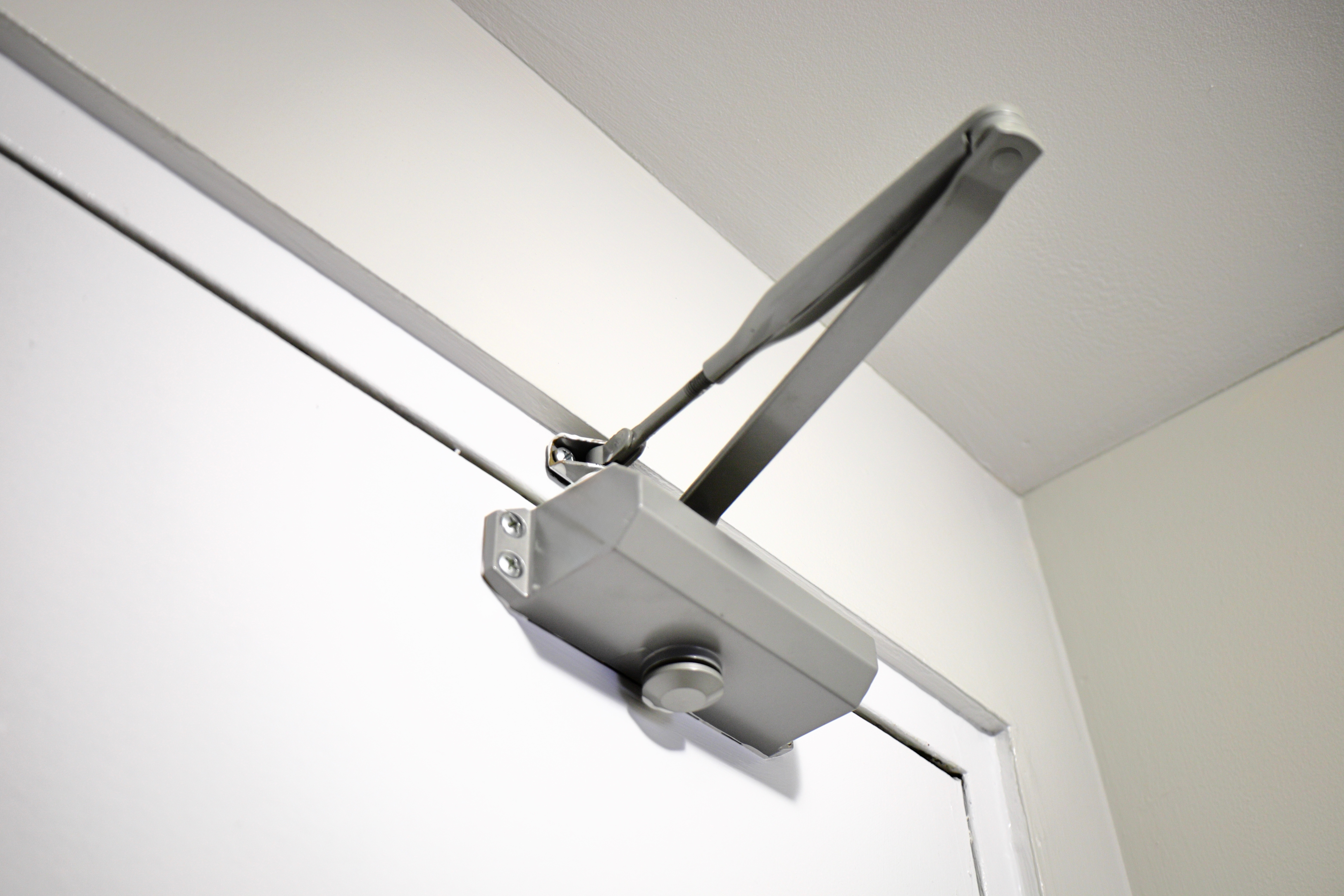 Silver automatic door closer mounted on top of white door frame